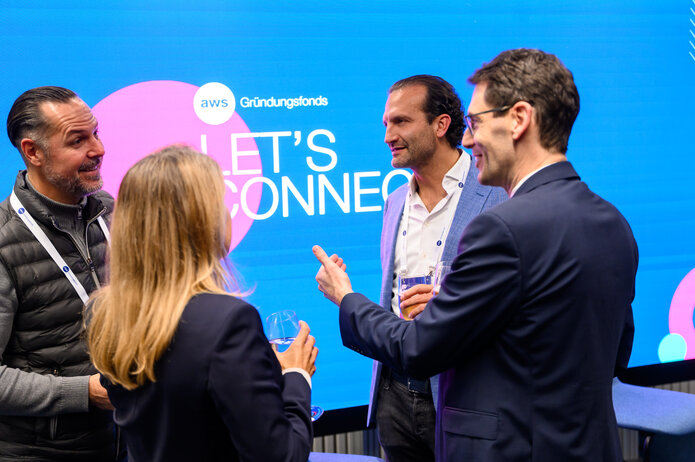 ruppe von Teilnehmern im Gespräch vor einem großen LED-Screen mit der Aufschrift „Let’s Connect“.