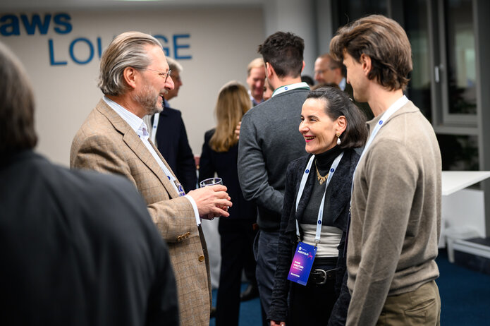 Teilnehmer im Gespräch während des Networkings in der aws Lounge. Mehrere Personen stehen zusammen und unterhalten sich.